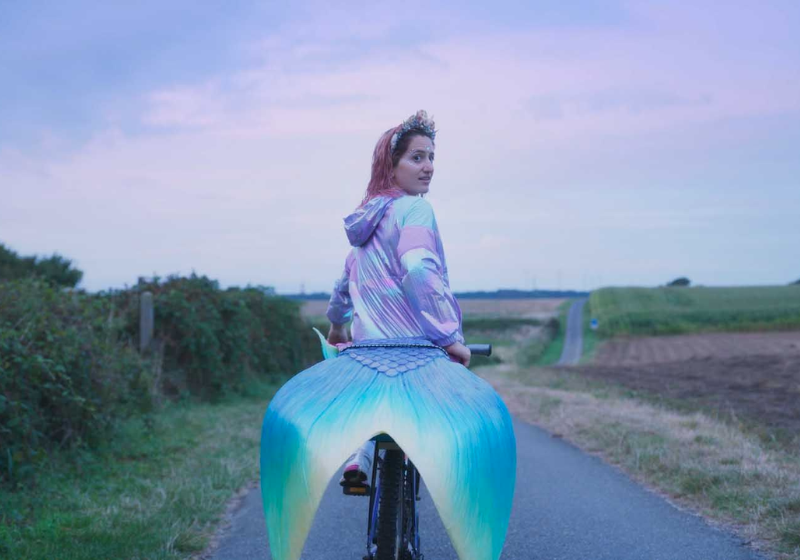 Une jeune femme avec une queue de sirène et sur un vélo.