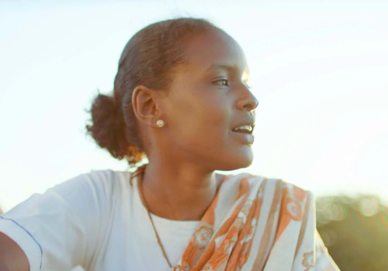 Une jeune femme les cheveux attachés en chignon, regarde sur la droite. Derrière le ciel est presque blanc.